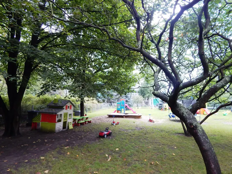 Zielony, ogrodzony plac zabaw przedszkola Czarodziejski Dworek wśród drzew